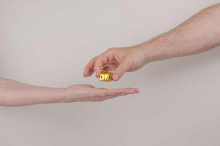 men holding a small gold ribbon wrapped gift box to female open hand on a white backdrop with copy space.の写真素材