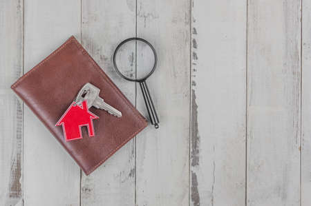 Metal keyring in the shape of a house with a metal key and magnifying glass on a white wood plank background. Real estate conceptの写真素材