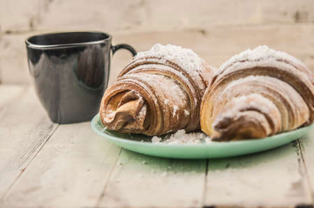 Two fresh croissants in plate on white wooden table. Breakfast