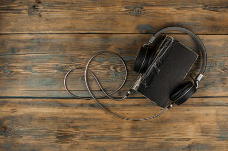 Audio book concept. Headphones and old book over wooden table. Top view with space for your text. Remote education concept.の写真素材