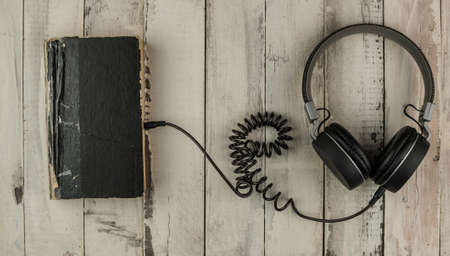 Audio book concept. Headphones and old book over wooden table. Top view with space for your text. Remote education concept.の写真素材