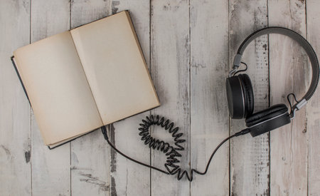 Open book with blank page and headphones on a wooden table. Remote education concept. Top viewの写真素材