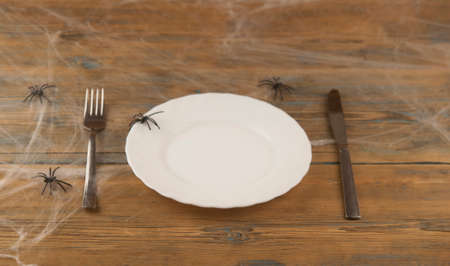 Halloween table setting blank dish, knife and fork with spider web on wood background. Trendy holiday concept.の写真素材