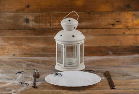 Halloween table setting blank dish, knife and fork with spider web on wood background. Trendy...