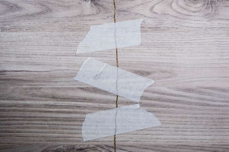 gray broken plywood board texture background with white masking tapeの写真素材