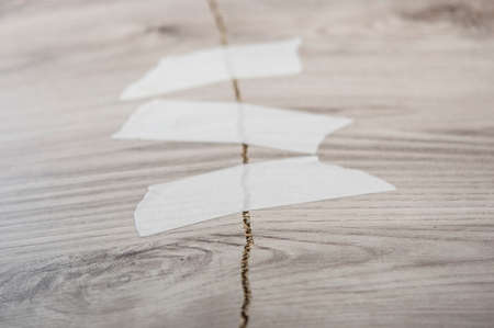 gray broken plywood board texture background with white masking tapeの写真素材