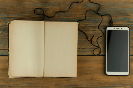 Black headphones with smarphone and open book are on the wooden table. Audio book concept. Distance learning. Close up, copy space, background.の写真素材