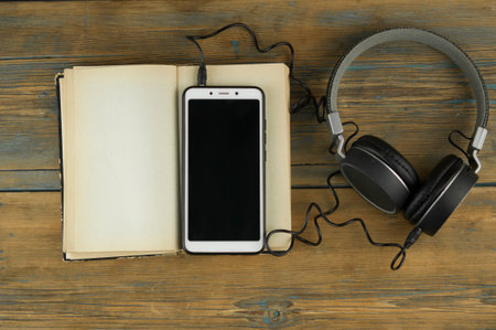 Black headphones with smarphone and open book are on the wooden table. Audio book concept. Distance learning. Close up, copy space, background.の写真素材