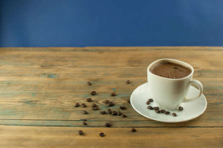 A cup of coffee on old wooden table with some roasted beans