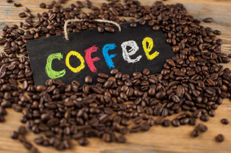 Heap coffee beans and a board with the inscription "coffee" written in a colorful alphabet. Coffee break, the concept of waking up in the morning. Top viewの写真素材