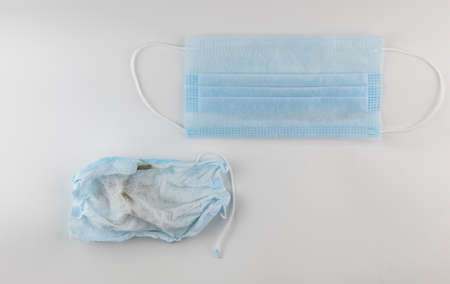 A used crumpled medical mask lies on a white background. There is a of new mask nearby.