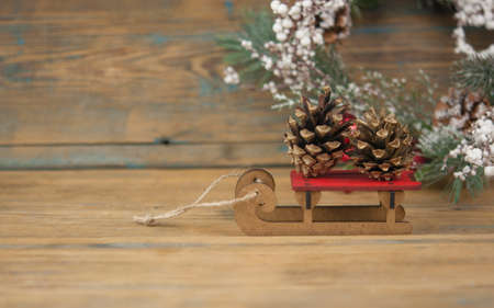 Toy wooden sled on wood background with fir cone, copy space. New year card.の写真素材