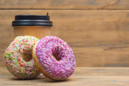 Yummy donuts with sprinkles and paper cup on wooden tableの写真素材