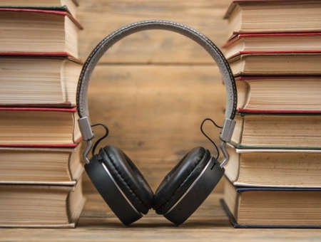 Stack of different color hardcover books with blank colorful covers and black headphones on table. Old versus new. Close up, copy space, background.の写真素材