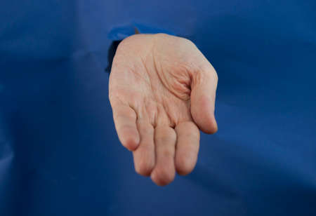 Female fist punching through blue paper background. War, struggle, conflict, feminist concept. Banner with copy space.の写真素材