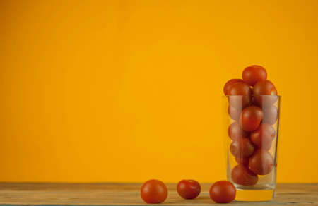 small red cherry tomatoes in a clear glass cup on a wood table background. red vegetablesの写真素材