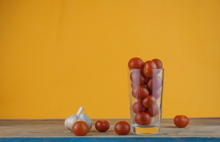 small red cherry tomatoes in a clear glass cup on a wood table background. red vegetablesの写真素材