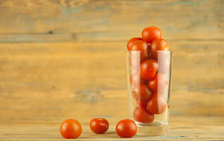 small red cherry tomatoes in a clear glass cup on a wood table background. red vegetablesの写真素材
