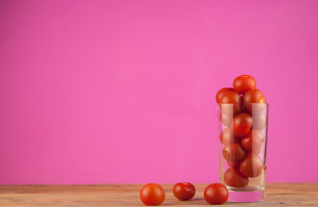 small red cherry tomatoes in a clear glass cup on a wood table background. red vegetables