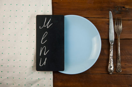 Menu written with chalk on aged blackboard with kitchen utinensil on wooden table. top viewの写真素材
