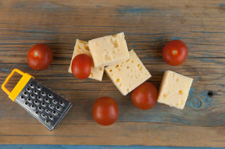 Stack cheese cubes and cherry tomatoes with miniature grater on a wood kitchen tableの写真素材