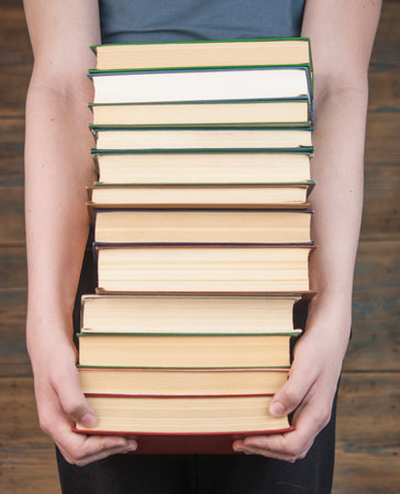Child holding a high pile of thick black books in his hands