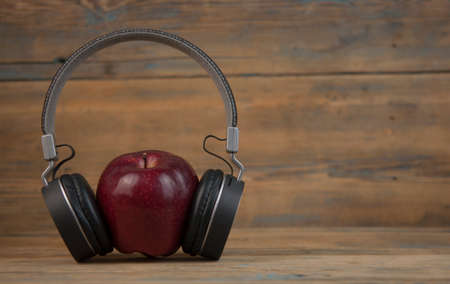 Abstract image with apples. One Apple in headphones on wooden background. audiobook. education onlineの写真素材