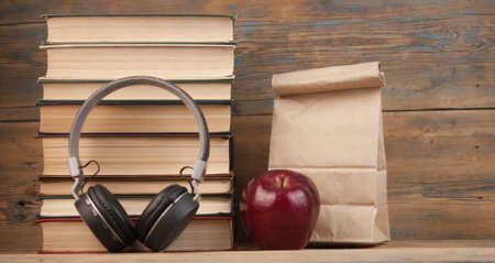 stack of books with red apple, lunch bag and headphone on the wood table with copyspaceの写真素材
