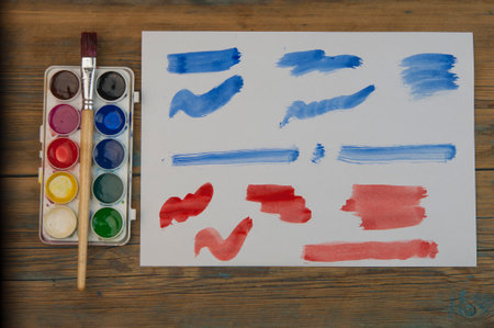 Paint brushes on old wooden background with colorful strokes on white paperの写真素材