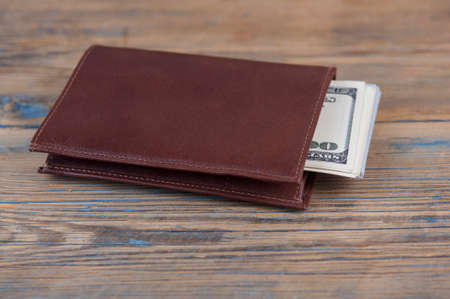 Brown leather wallet with one hundred dollar bills on wooden table. ortune conceptの写真素材