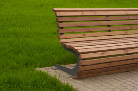 Empty wood bench on green grass in the city park during summer sunny day. Public chair on the lawn in scenic meadow and garden.の写真素材