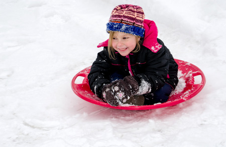 Happy child sledding down a hill on a saucer sledの写真素材