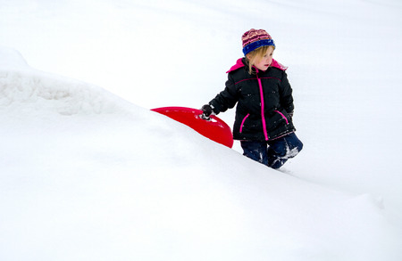 little girl with red sled playing in the snowの写真素材