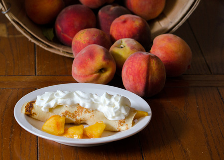 peach crepes with whipped cream and a basket of fresh peachesの写真素材