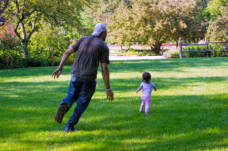 A dad chases after his active little toddler as they run in a parkの写真素材