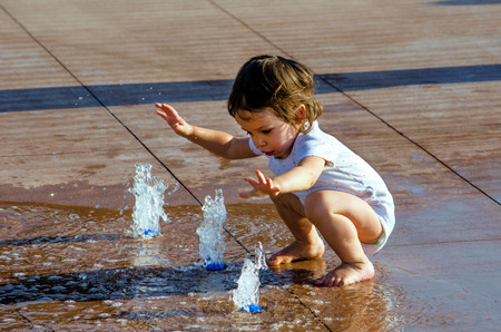 A toddler plays in a fountain for children located in a city areaの写真素材