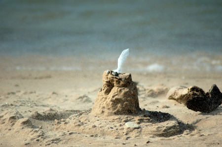 A sea gull feather crowns the top of this simple sand castle on a windy beach near lake michigan の写真素材