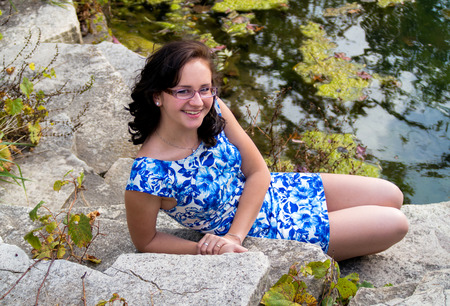 pretty teen age girl sitting on the rocks by a lakeの写真素材