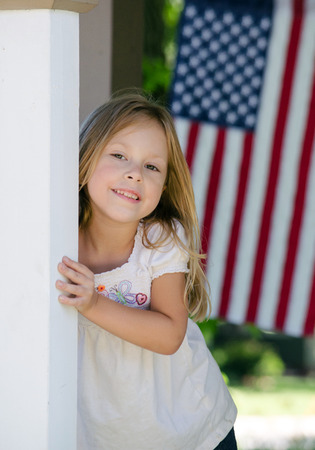 little blond girls on a porch with an American flagの写真素材