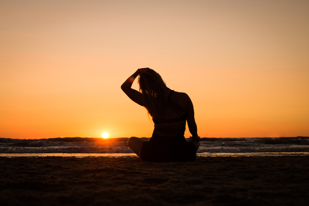 Silhouette of a girl practicing yoga on the beach at sunsetの写真素材