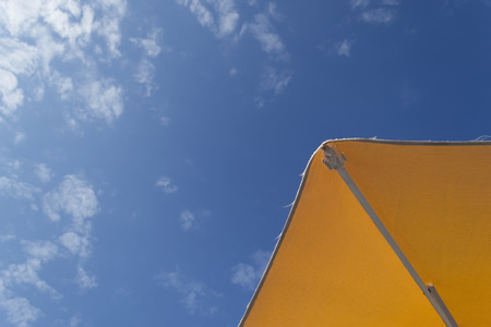 Orange sun umbrella under a clear blue summer sky with a few white cloudsの写真素材