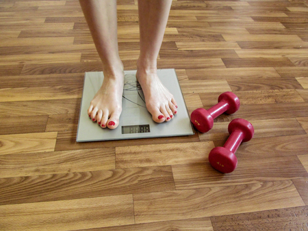 Two slender female legs stand on electronic scales. And two red dumbbells on the floor near the scales hint that the girl needs to watch the weightの写真素材