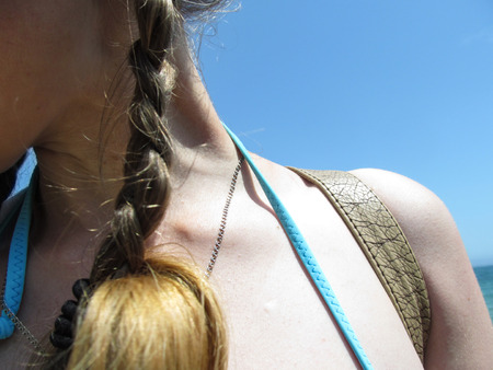 Female naked neck, shoulder and hair in a pigtail close-up against a blue sky. A girl in a swimsuit resting on the sea - concept, abstractの写真素材