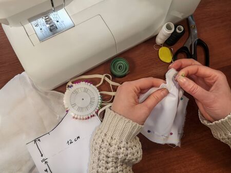 Seamstress holds fabric together with ball-point pins. Female hands pin a pattern of a medical face...