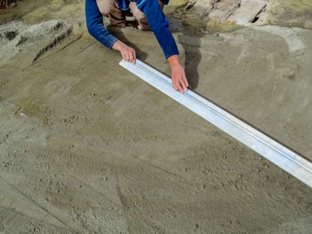 The builder smooths the surface of a dry sand-cement mortar with a long metal plank for laying...