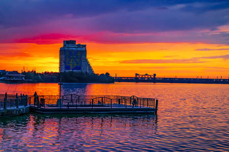 Dnipro, Ukraine - July 20, 2020: Hotel Parus in Dnipro against the background of a sunset reflected in the water of the Dnieper river. Beautiful evening orange-purple cityscapeのeditorial素材