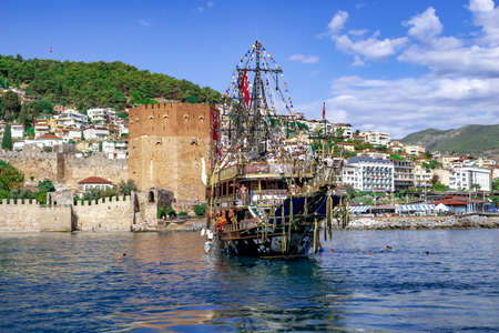 Turkey, Alanya - October 22, 2020: Pirate schooner near the Red Tower in Alanya. Beautiful seascape with Kizil Kule building on the background of the mountain and a tourist big ship in blue waterのeditorial素材