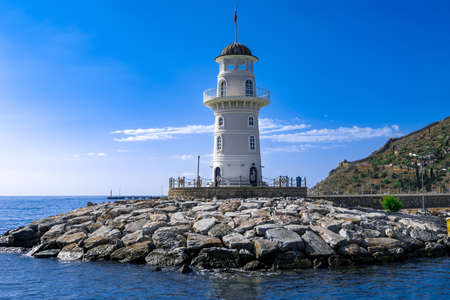 Alanya Deniz Feneri close-up, view from the sea. White vintage lighthouse on the stone coast against the background of the blue Mediterranean sea and mountains in the Turkish resortの写真素材