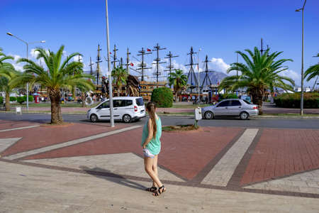 A young tourist girl looks at the masts of pirate ships on the waterfront in Alanya (Turkey). Travel...