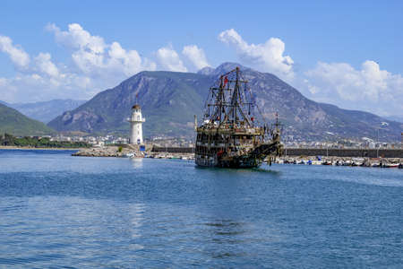 Turkey, Alanya - October 22, 2020: Pirate vintage ship in the Mediterranean Sea against of Alanya Lighthouse and a large mountain on the shore. Beautiful seascape with old schooner in blue waterのeditorial素材